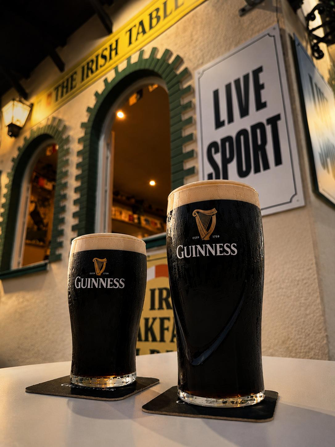 Two perfectly poured pints of Guinness outside The Irish Table with Live Sport signage